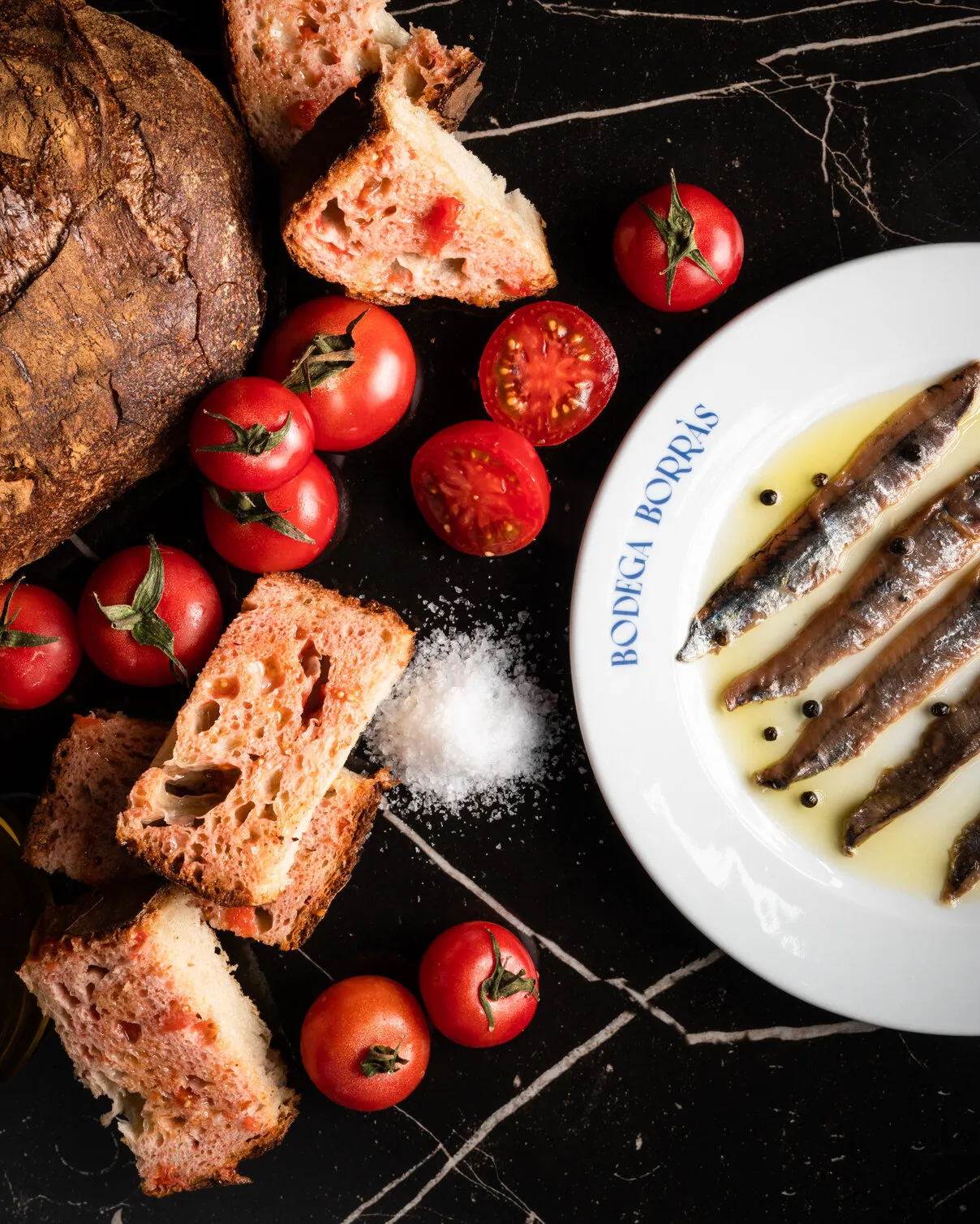 Anchoas, pan y tomates sobre mármol negro
