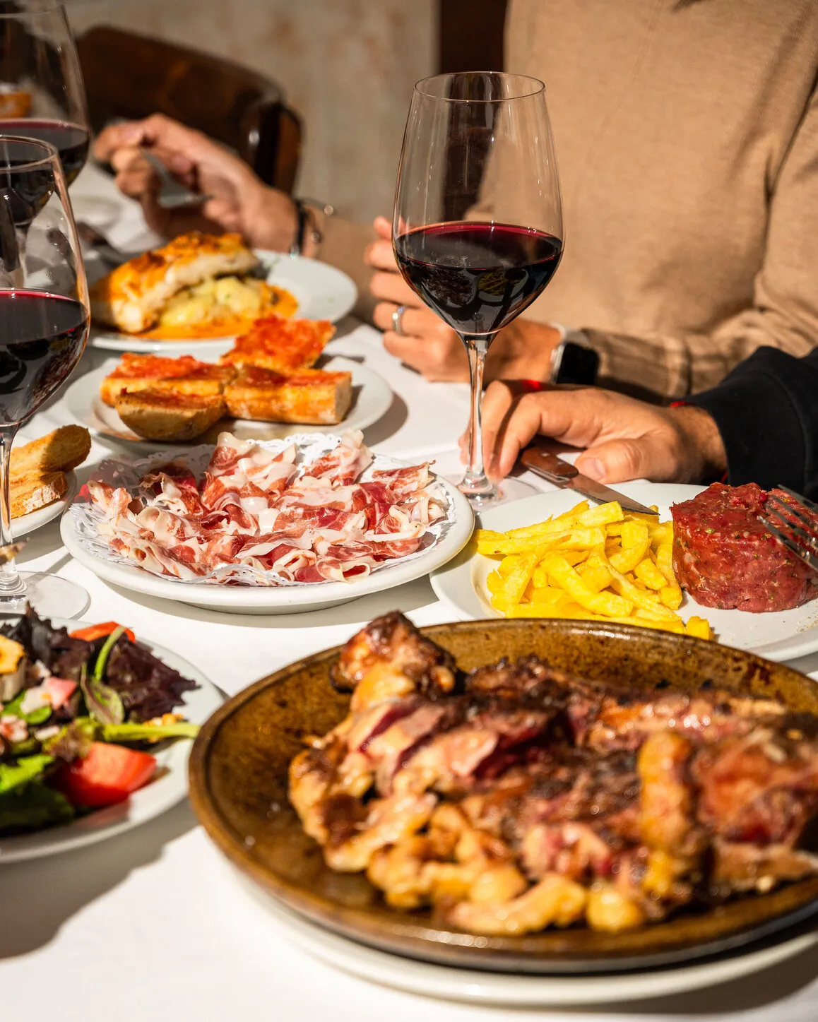 Mesa compartida llena de platos y copas de vino
