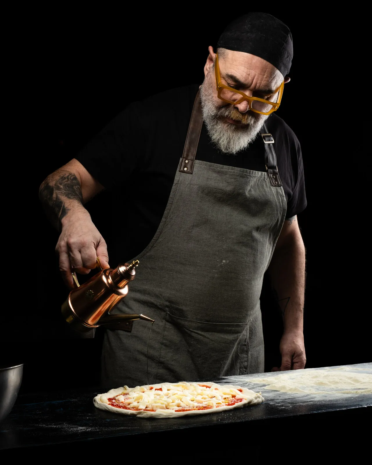 Pizzero aliñando una pizza recién hecha