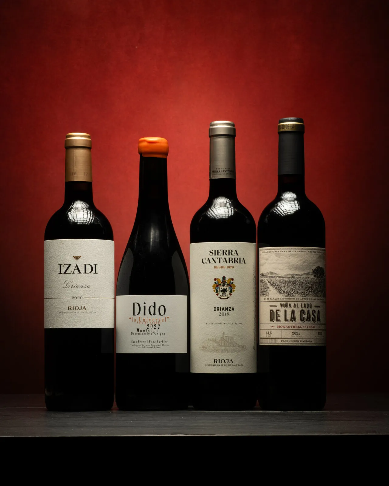 Cuatro botellas de vino tinto sobre fondo rojo